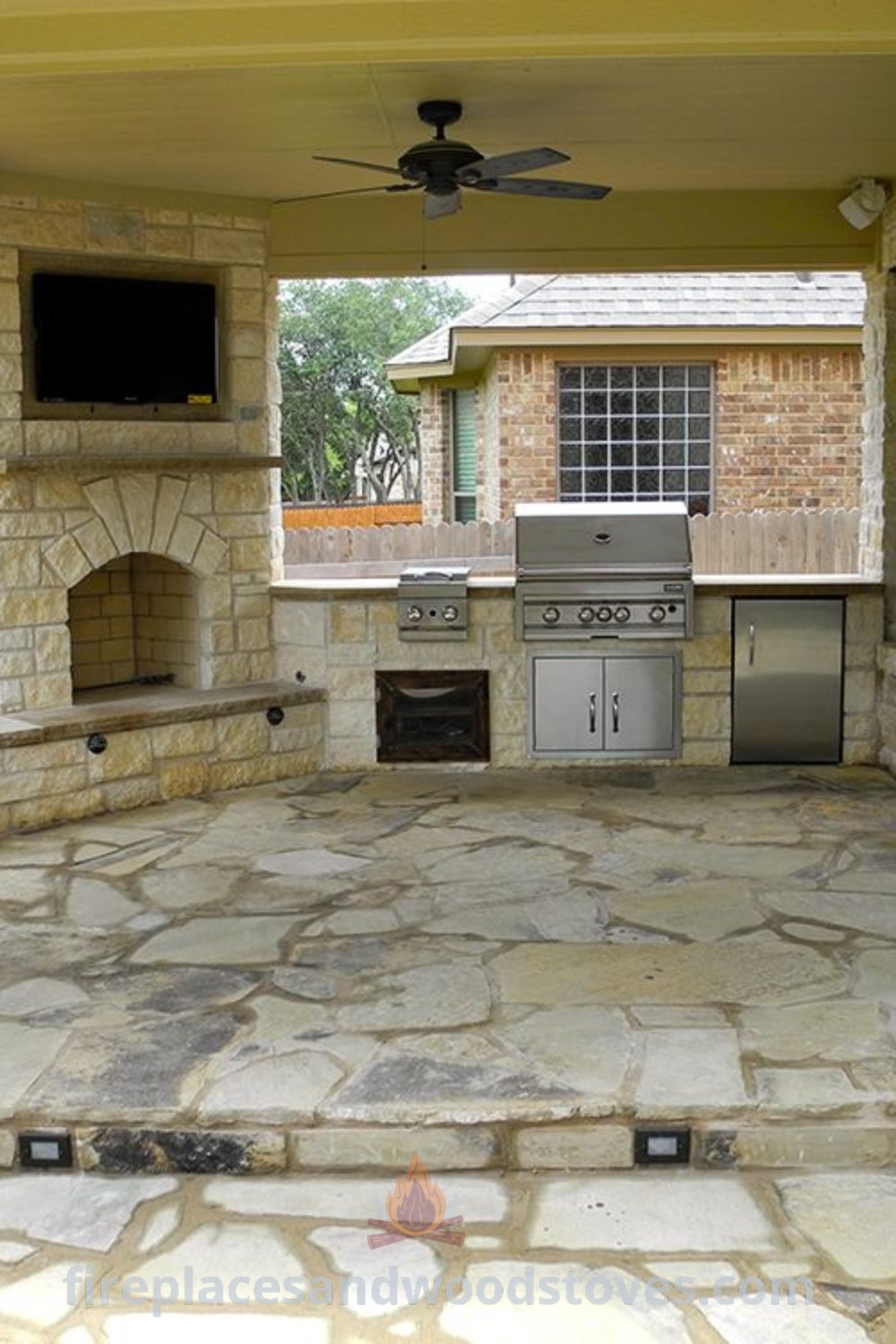An outdoor kitchen and grill area with stone flooring under a covered patio, featuring a cozy fireplace and stylish design. Perfect for outdoor cooking and entertaining, this setup offers incredible ideas for transforming your backyard. Discover more outdoor inspirations at patioandhomefurniture.com.
