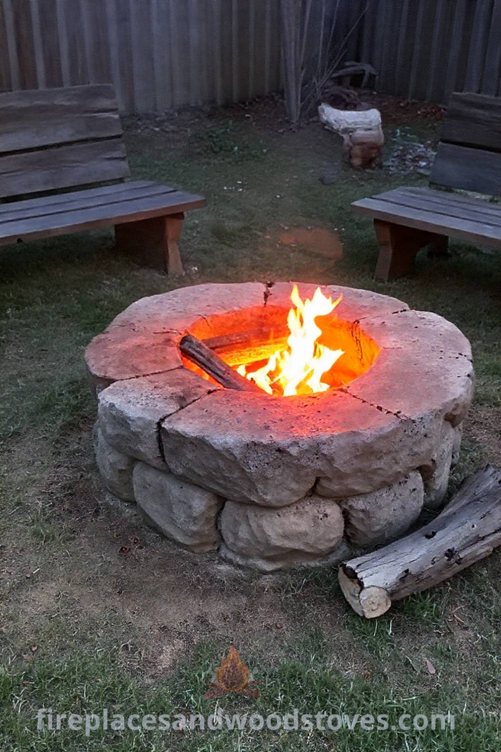 Stone fire pit at the center of a cozy backyard, surrounded by wooden benches and a warm glow from flickering flames, creating an inviting gathering space. Visit patioandhomefurniture.com for stylish outdoor ideas transforming your backyard into a dream retreat.