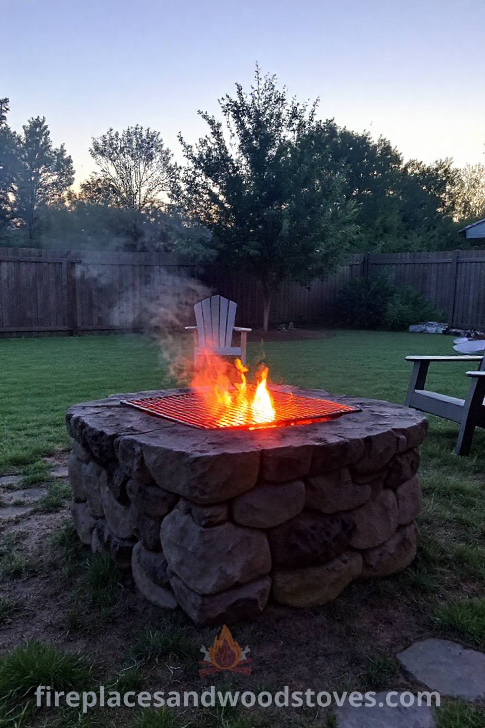 Stone charcoal fire pit in a cozy backyard setting, surrounded by chairs and a patch of grass, showcasing a warm ambiance for gatherings and storytelling. Visit patioandhomefurniture.com for stylish ideas transforming your backyard into a dream space for unforgettable moments.