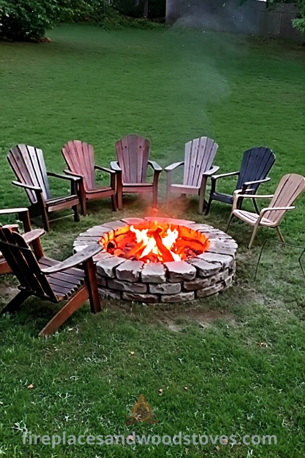Stone fire pit in a grassy backyard surrounded by mismatched chairs, creating a cozy and inviting space for gatherings, perfect for storytelling under the stars. Visit patioandhomefurniture.com for incredible outdoor design ideas that will wow your guests.