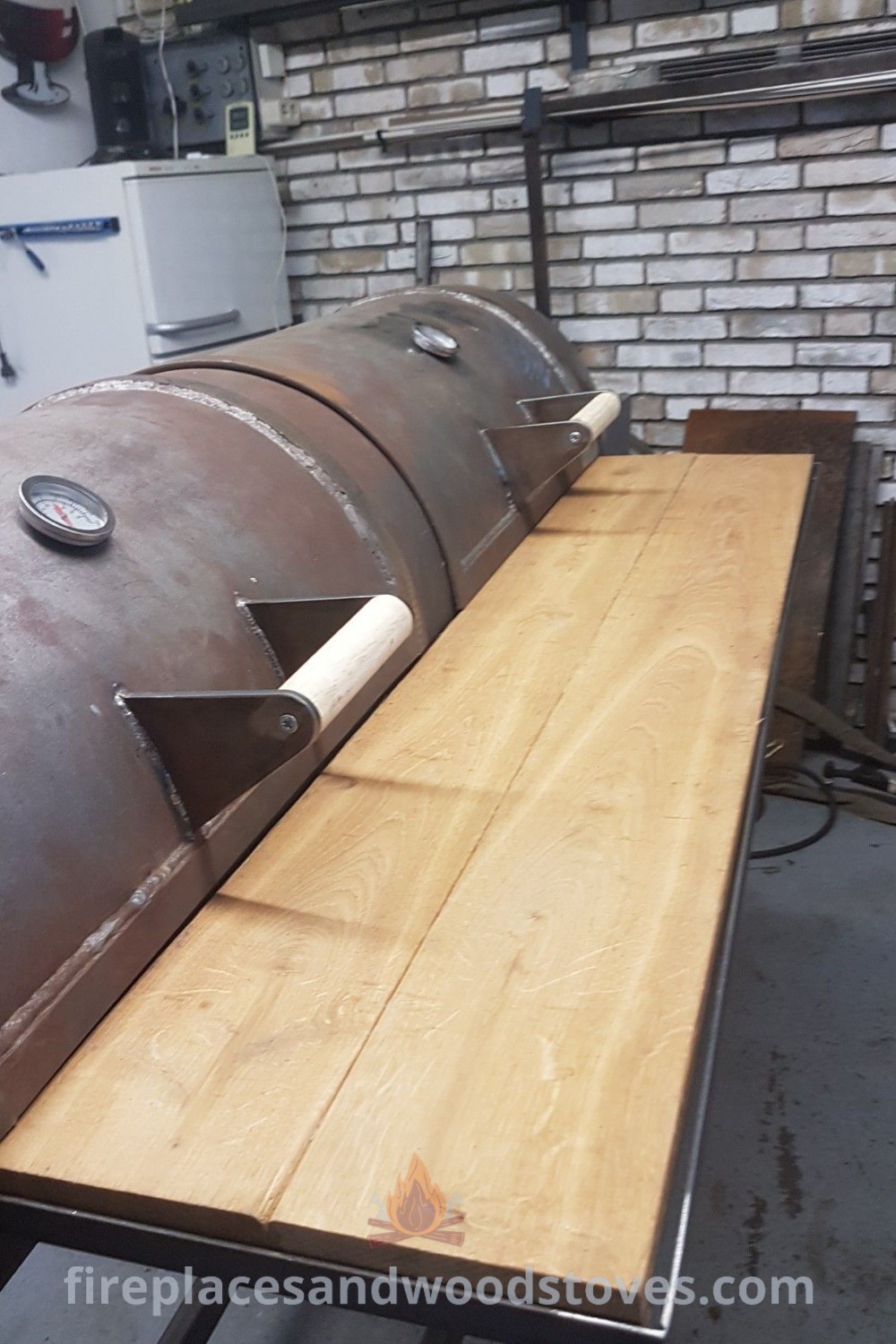 A large custom BBQ smoker made of metal, elegantly displayed on a wooden table with brick walls in the background, showcasing stylish designs for outdoor cooking. Discover more incredible ideas for your backyard at patioandhomefurniture.com.