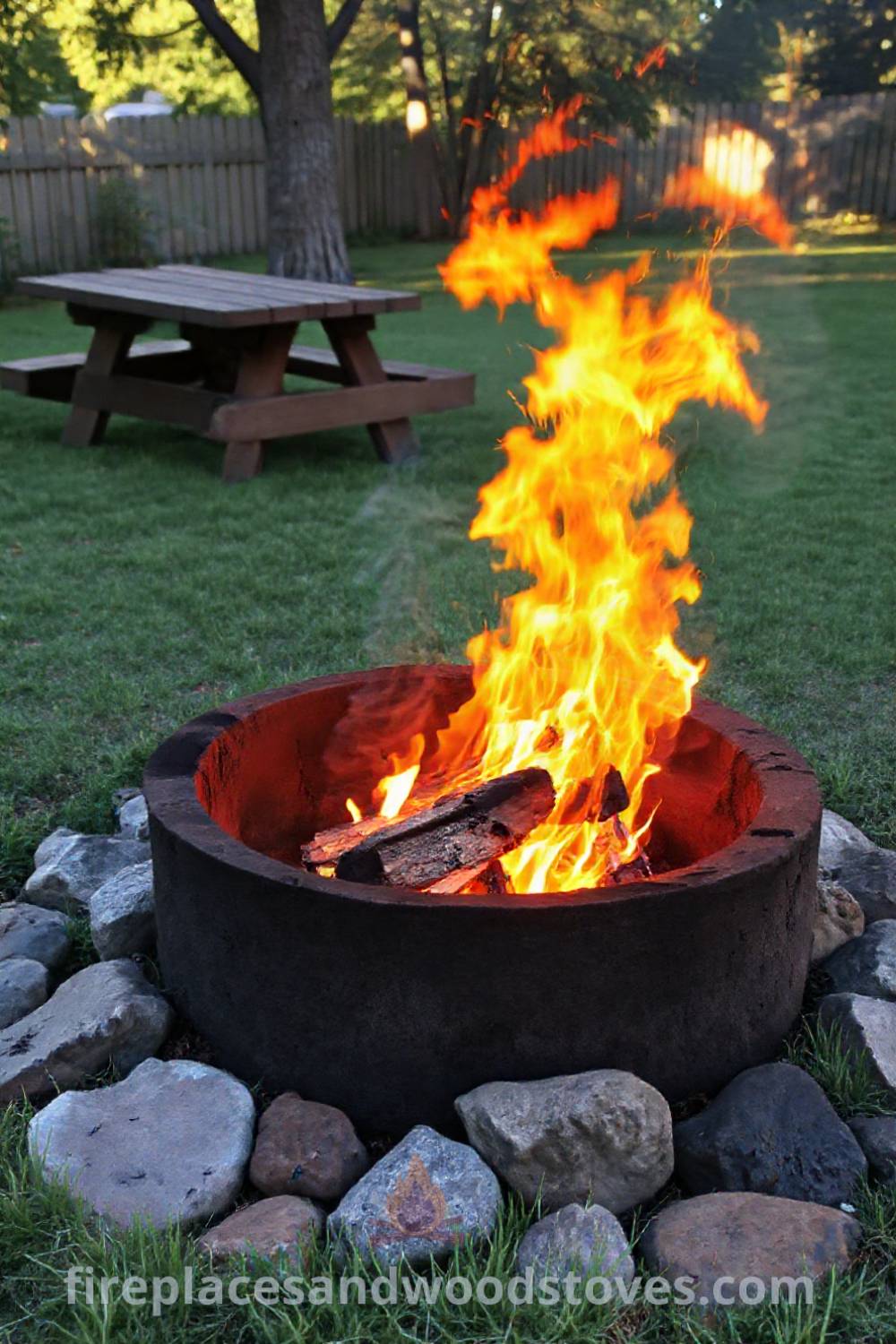 A rustic charcoal camping fire pit nestled in a grassy backyard with sun-warmed stones, creating a cozy atmosphere for outdoor gatherings. Visit patioandhomefurniture.com for stylish designs transforming your backyard into an inviting space.