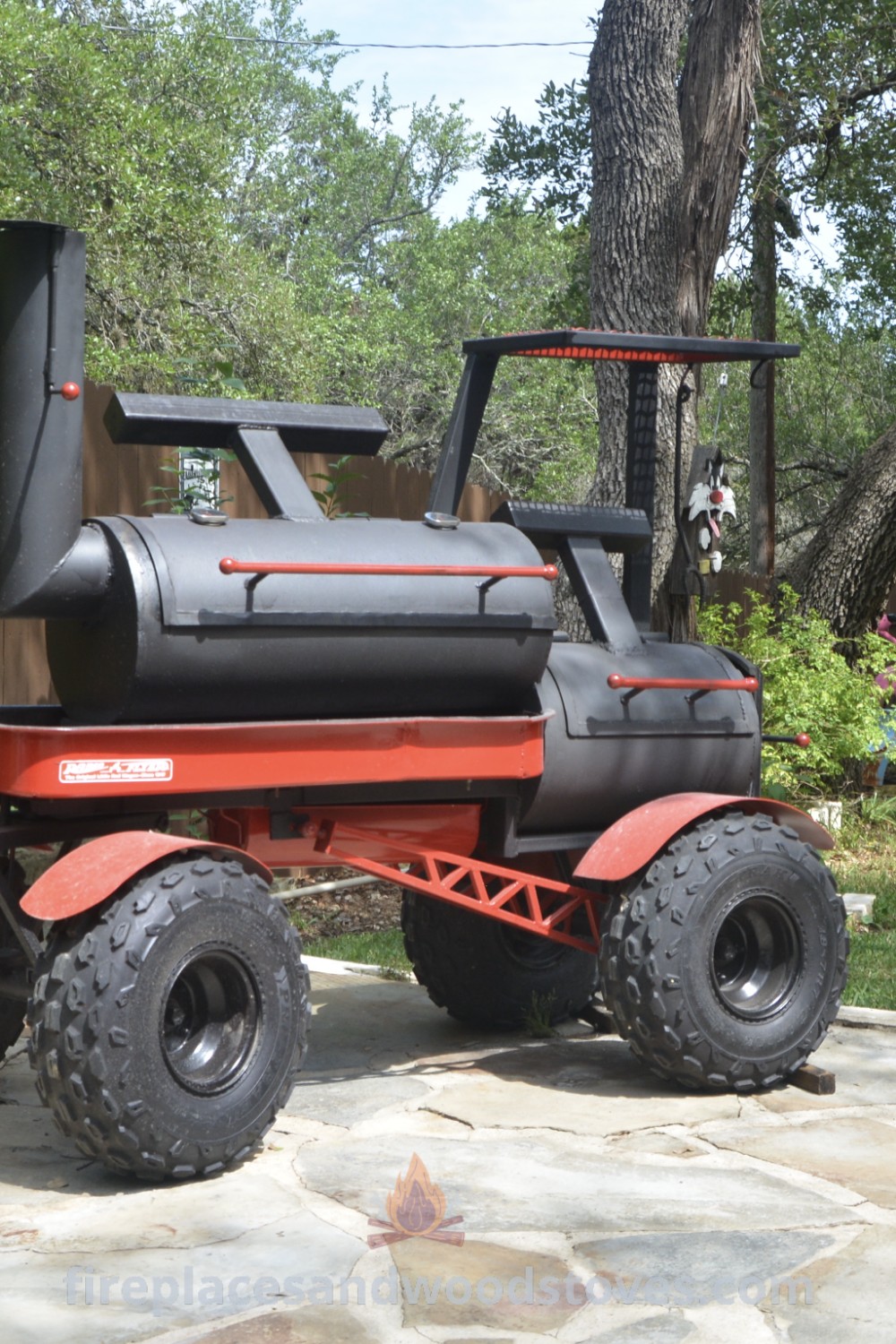 A red and black cart BBQ pit sitting on a stone patio next to a tree, showcasing stylish designs for backyard entertaining. Discover DIY ideas and custom BBQ grill options at patioandhomefurniture.com.