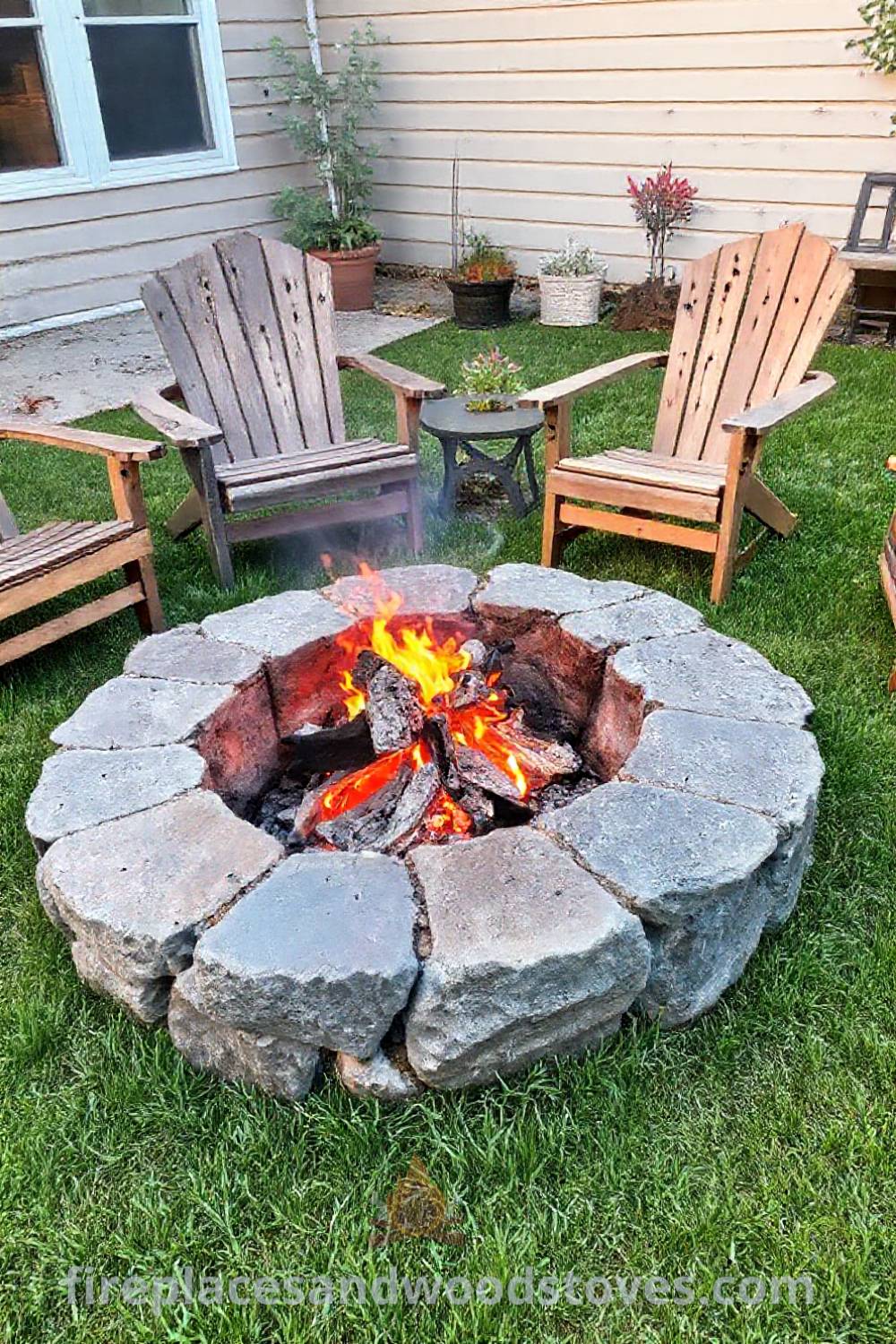 Backyard stone fire pit designed for charcoal grilling surrounded by mismatched wooden chairs, creating a cozy outdoor gathering space with lush grass and potted plants, ideal for intimate moments. Visit patioandhomefurniture.com for stylish outdoor design inspiration.