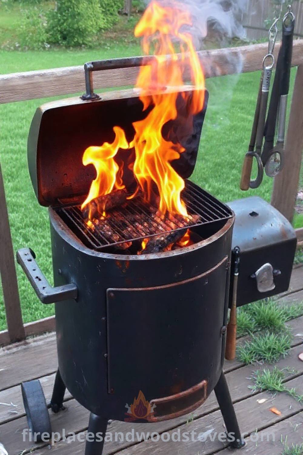 Sturdy barbecue smoker on a wooden deck with flames emanating from the firebox, surrounded by green grass and an array of tools, creating a cozy outdoor cooking space that inspires stylish backyard designs. Visit patioandhomefurniture.com for incredible ideas that will wow your guests.