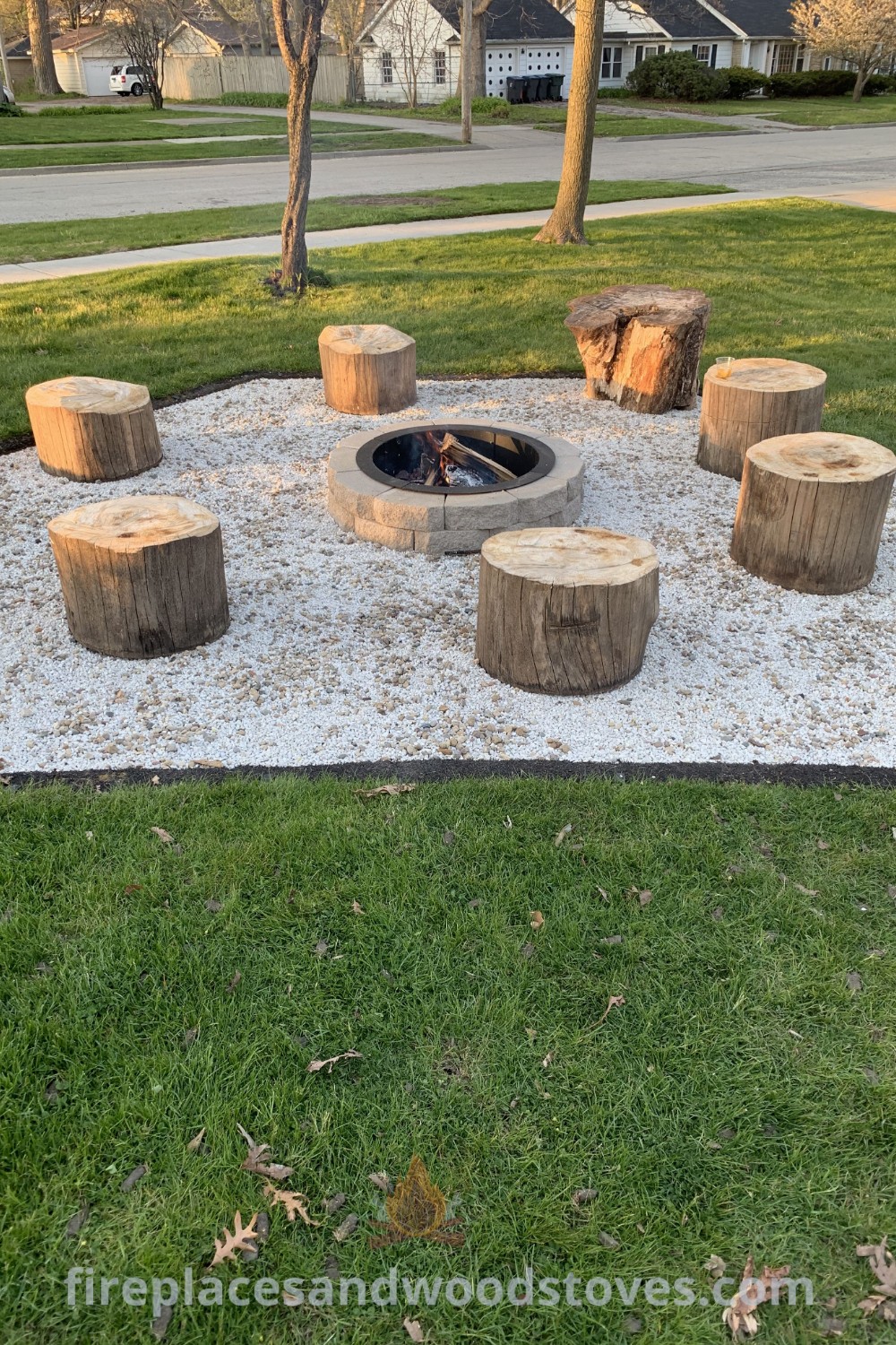 An outdoor fire pit surrounded by logs and gravel, featuring tree stump seating for a cozy gathering space. A stylish setup that combines function and aesthetic, perfect for creating memorable outdoor experiences. Explore more ideas at patioandhomefurniture.com.