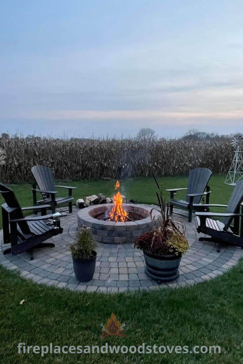 A fire pit with chairs surrounding it in the middle of a grassy field at dusk, showcasing a stylish backyard fire pit design on pavers, perfect for cozy outdoor gatherings. Discover incredible fire pit ideas at patioandhomefurniture.com.