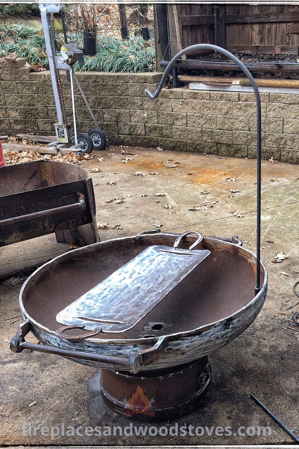 A creative propane tank fire pit surrounded by an old metal wheelbarrow, ideal for outdoor fire cooking and enhancing your backyard with stylish designs. Discover more incredible ideas at patioandhomefurniture.com.