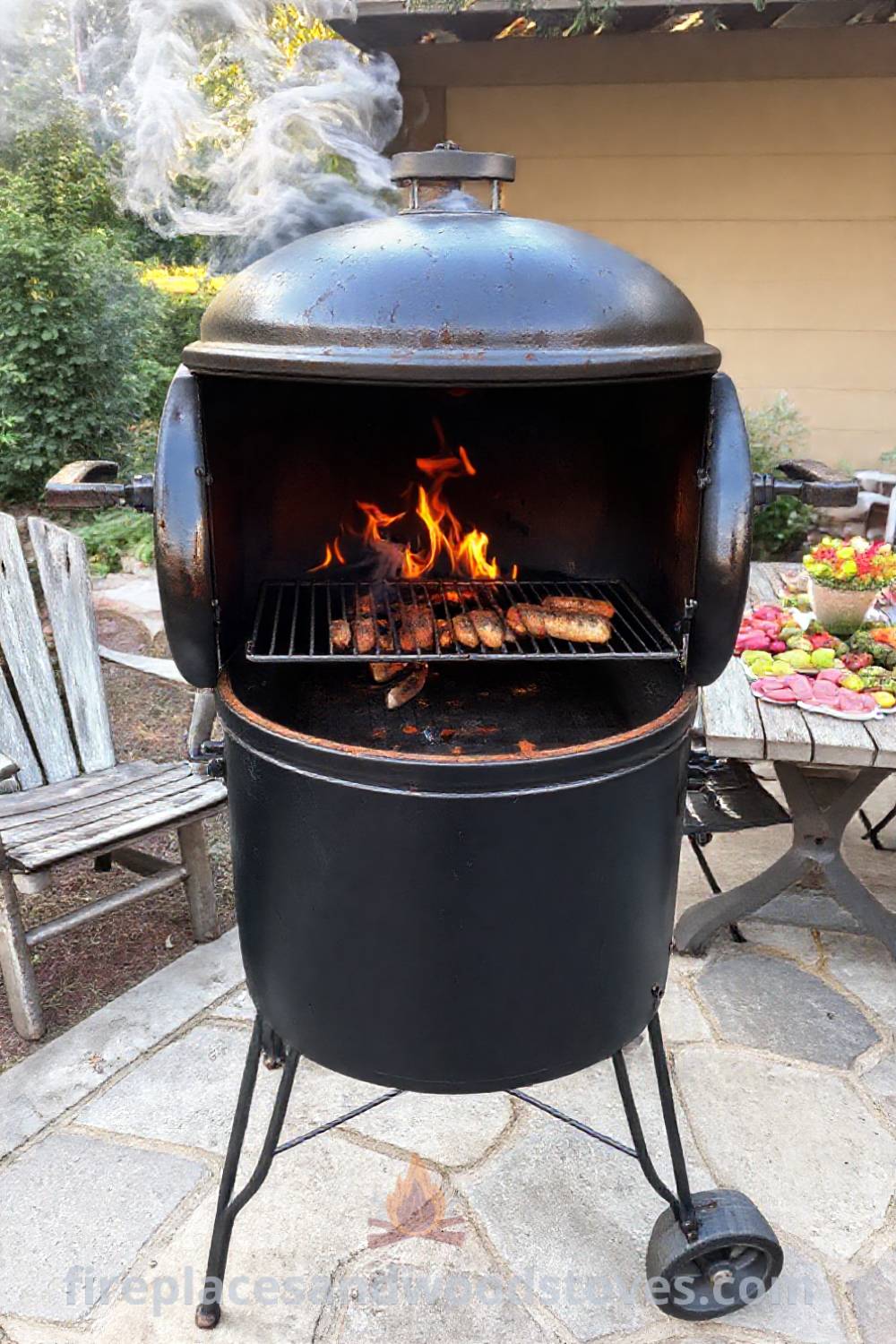 Black steel barbecue smoker on a stone patio surrounded by mismatched lawn chairs and a wooden table filled with fresh ingredients, creating a cozy outdoor atmosphere perfect for gatherings. Discover stylish outdoor designs transforming your backyard at patioandhomefurniture.com.