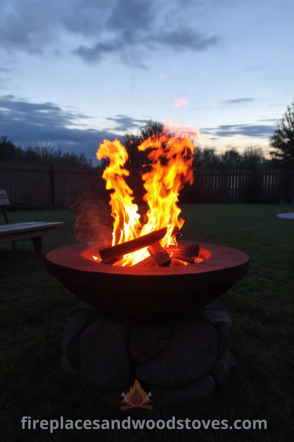 Backyard wood-burning fire pit on a stone base surrounded by grassy area and wooden benches, creating a cozy atmosphere for gatherings, perfect for outdoor relaxation. Visit patioandhomefurniture.com for stylish designs transforming your backyard into a dream space.