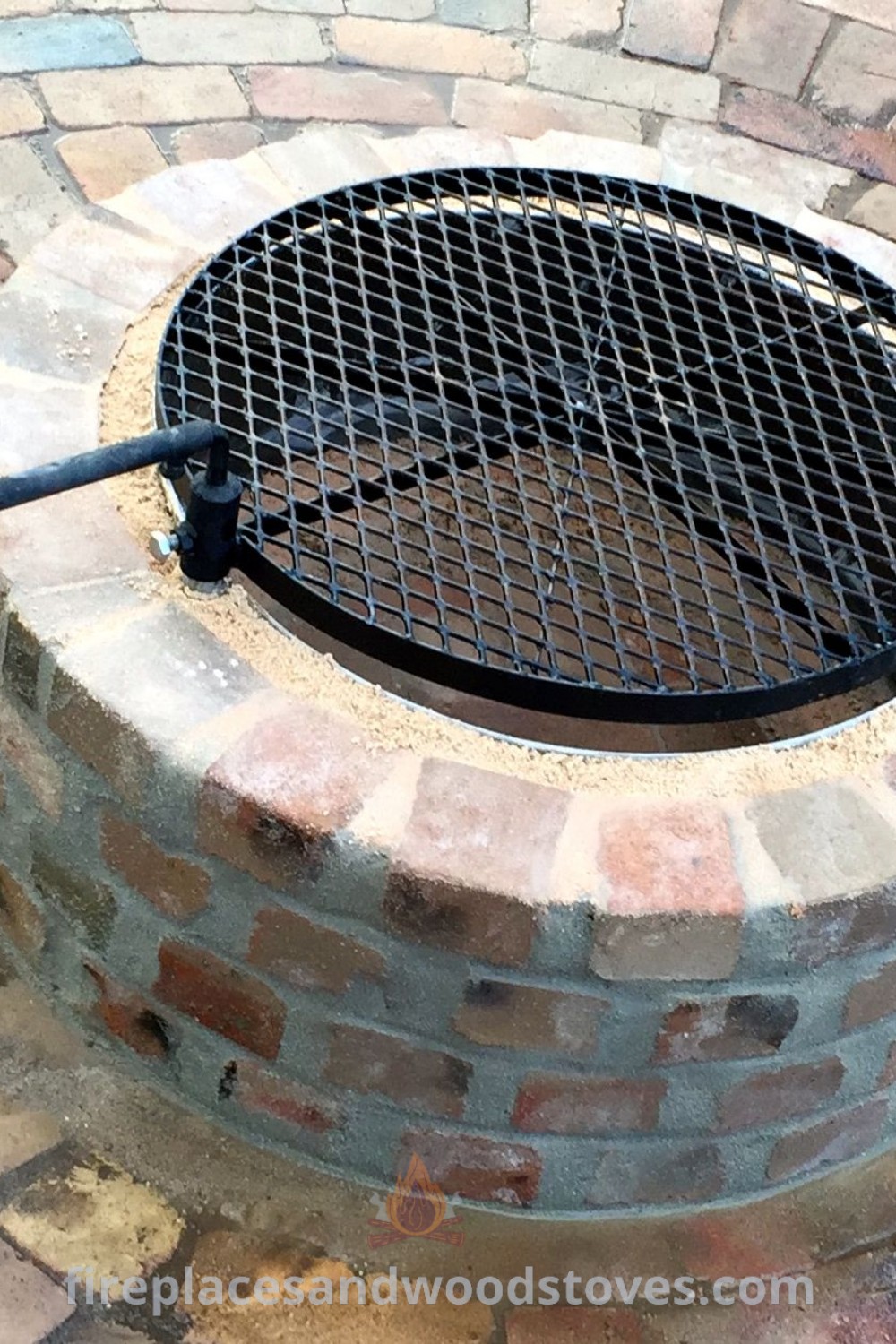 A brick fire pit on a stone patio alongside a metal grate, showcasing garden fire pit ideas and outdoor fireplace designs. Perfect for cozy evenings and multifunctional outdoor living, explore more styles at patioandhomefurniture.com.