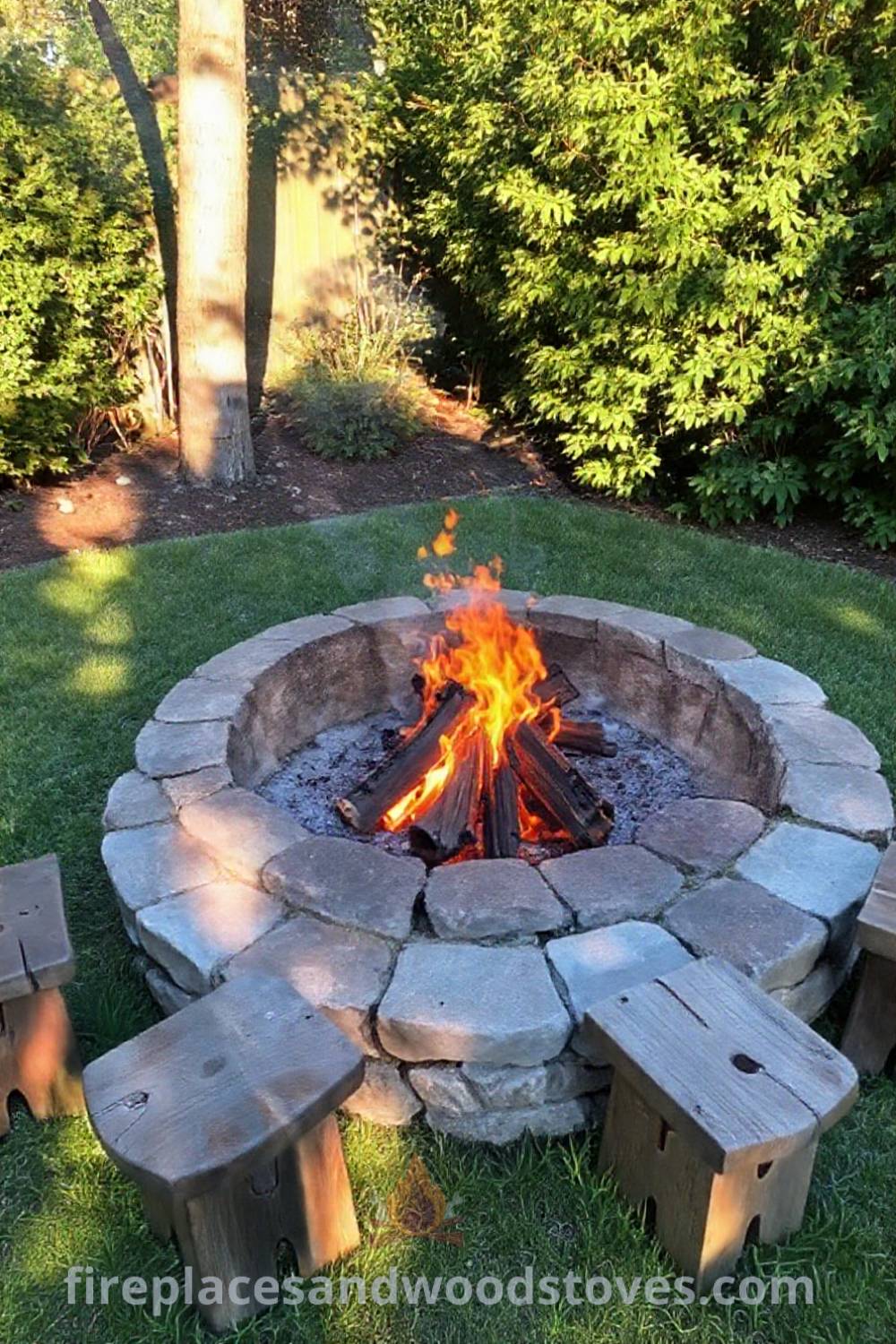Circular stone fire pit nestled in a lush backyard, surrounded by wooden stools, creating a cozy and inviting atmosphere for gatherings. Visit patioandhomefurniture.com for stylish outdoor design inspiration.