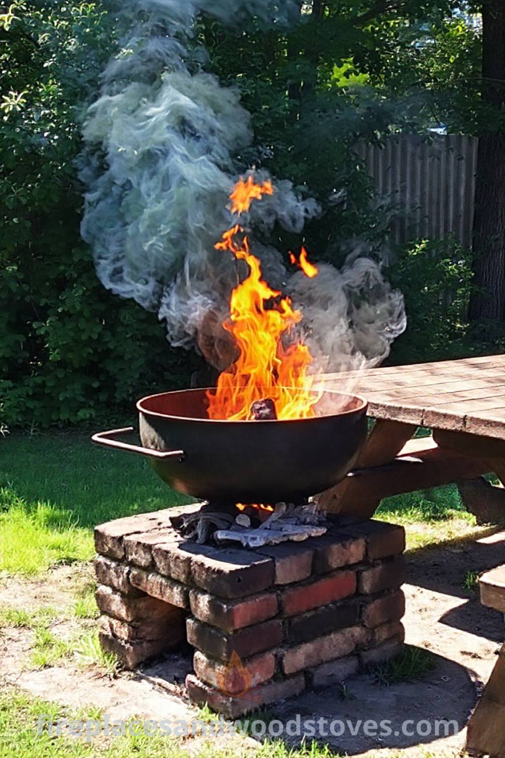 Wood-fired barbecue in a sunlit backyard with an uneven brick base, surrounded by greenery, creating a cozy and inviting outdoor atmosphere for gatherings. Visit patioandhomefurniture.com for stylish outdoor ideas that will wow your guests.
