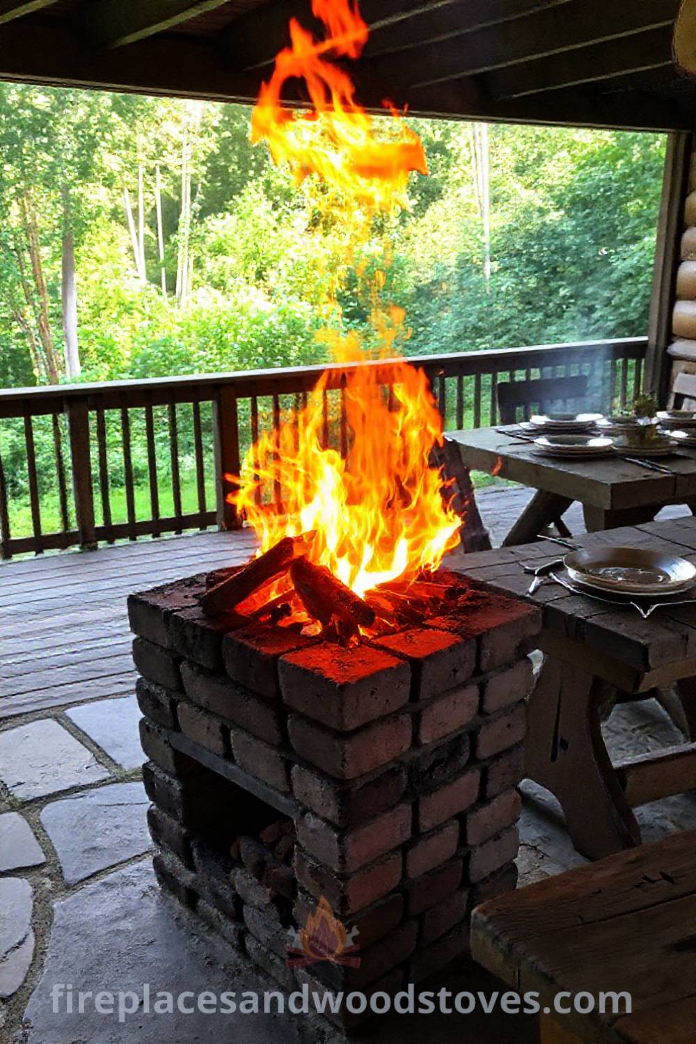 Rustic wood-fired barbecue on a stone patio with warm flames, surrounded by lush greenery and a wooden table set with mismatched plates and utensils, creating a cozy outdoor gathering space. Visit patioandhomefurniture.com for stylish designs transforming your backyard.