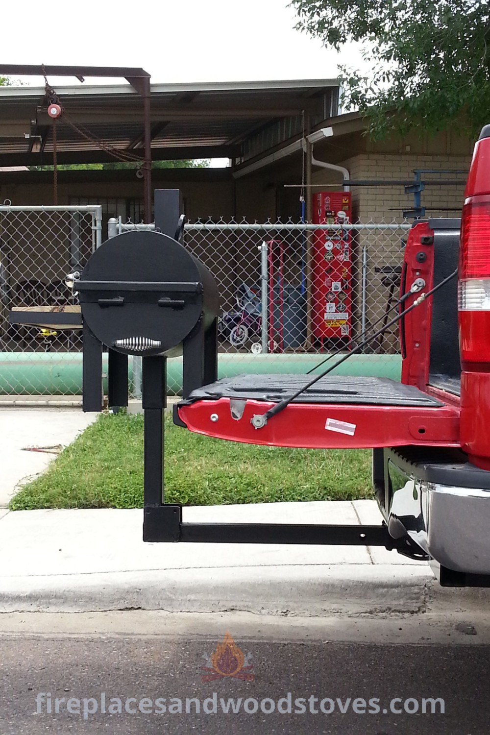 The back end of a red pickup truck parked in front of a building with a portable BBQ grill attached. Ideal for outdoor cooking, showcasing BBQ equipment tools and propane tank BBQ grills. Find more inspiring ideas at patioandhomefurniture.com.