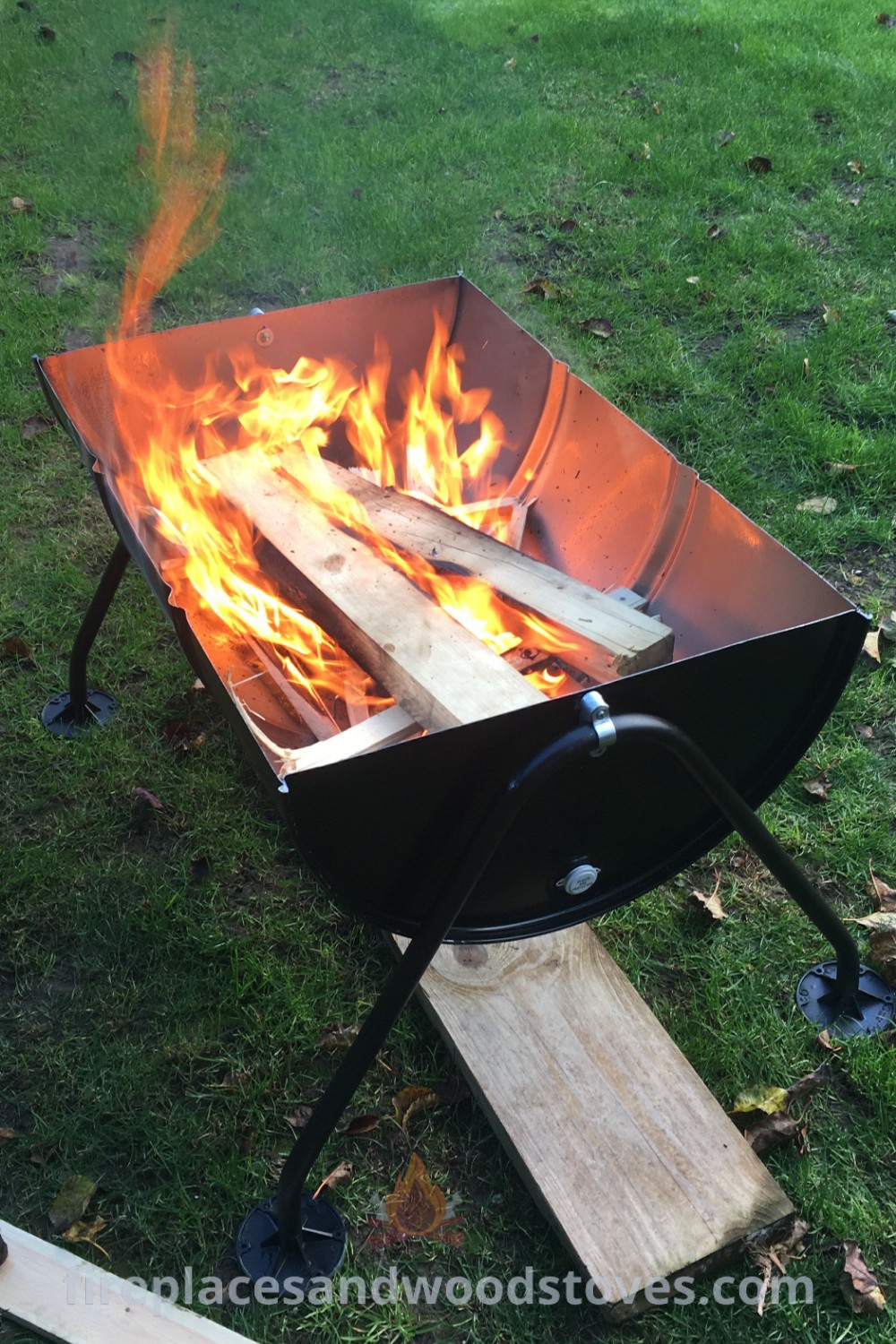 A stylish oil drum fire pit burning flames in the grass, perfect for cozy outdoor gatherings. Discover incredible designs transforming your backyard at patioandhomefurniture.com.