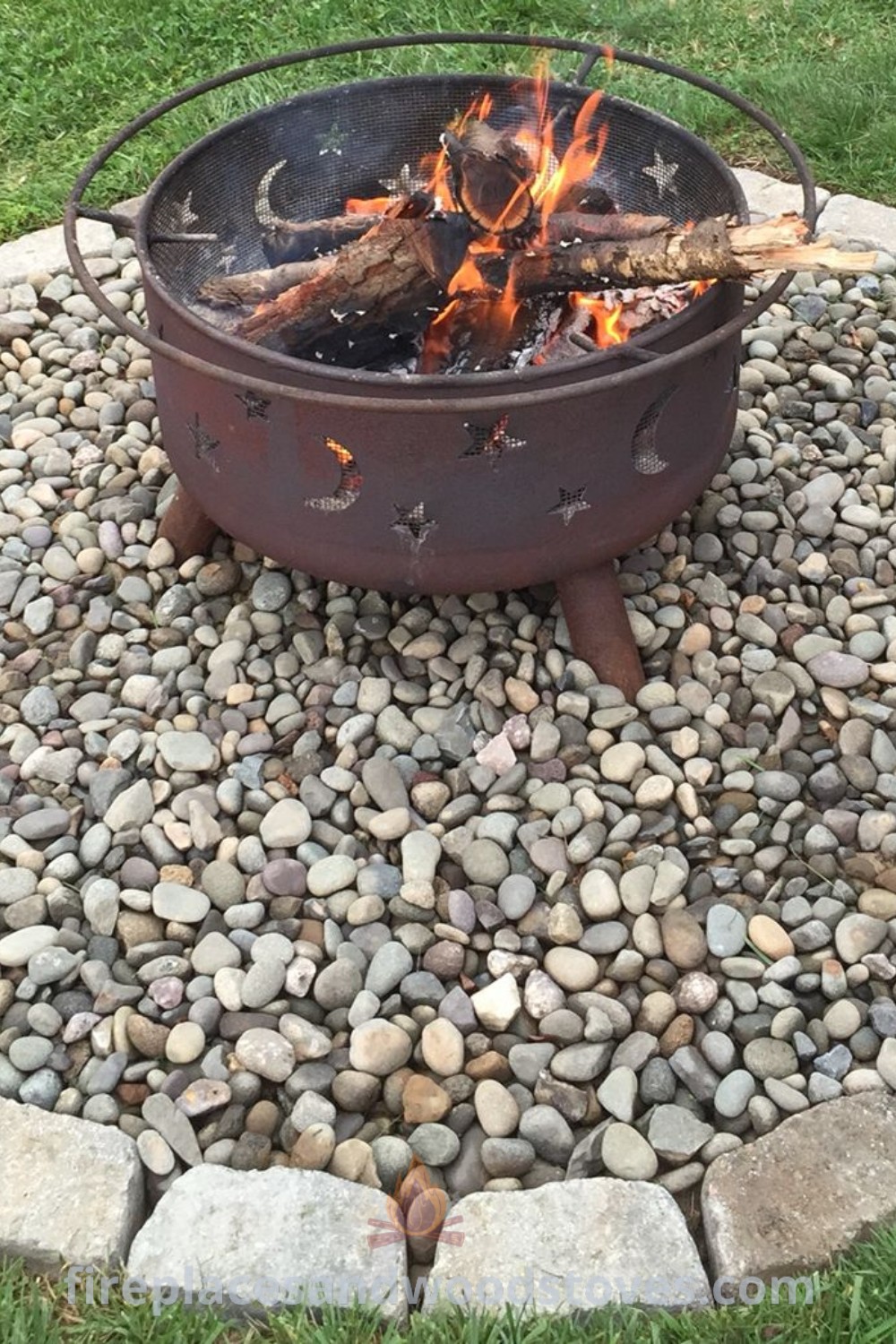 A river rock fire pit sitting on a lush green field, providing a stylish and cozy outdoor gathering space. Discover incredible designs and ideas for your backyard at patioandhomefurniture.com.