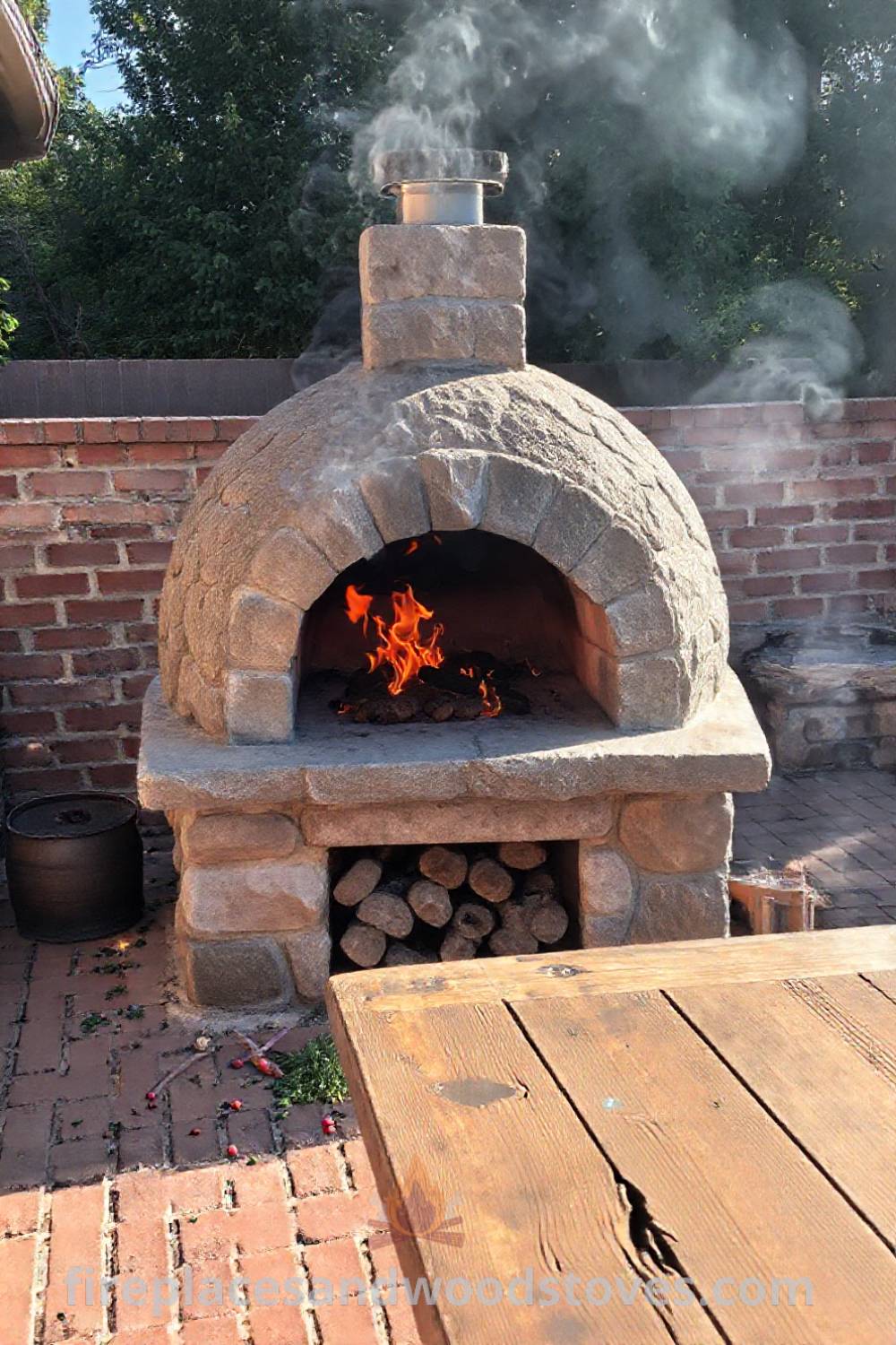 Sturdy stone BBQ oven on a brick patio, surrounded by herbs and spices, with a cozy ambiance created by flames, perfect for outdoor gatherings. Visit patioandhomefurniture.com for incredible outdoor design inspiration.