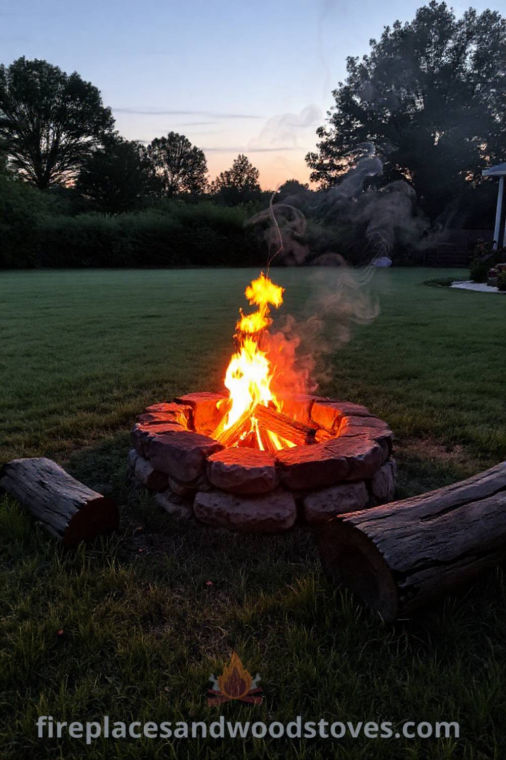 Cozy stone fire pit in a lush backyard surrounded by grass and wooden logs, creating an inviting atmosphere for gatherings. Visit patioandhomefurniture.com for stylish outdoor design inspiration with incredible ideas that will wow your guests.
