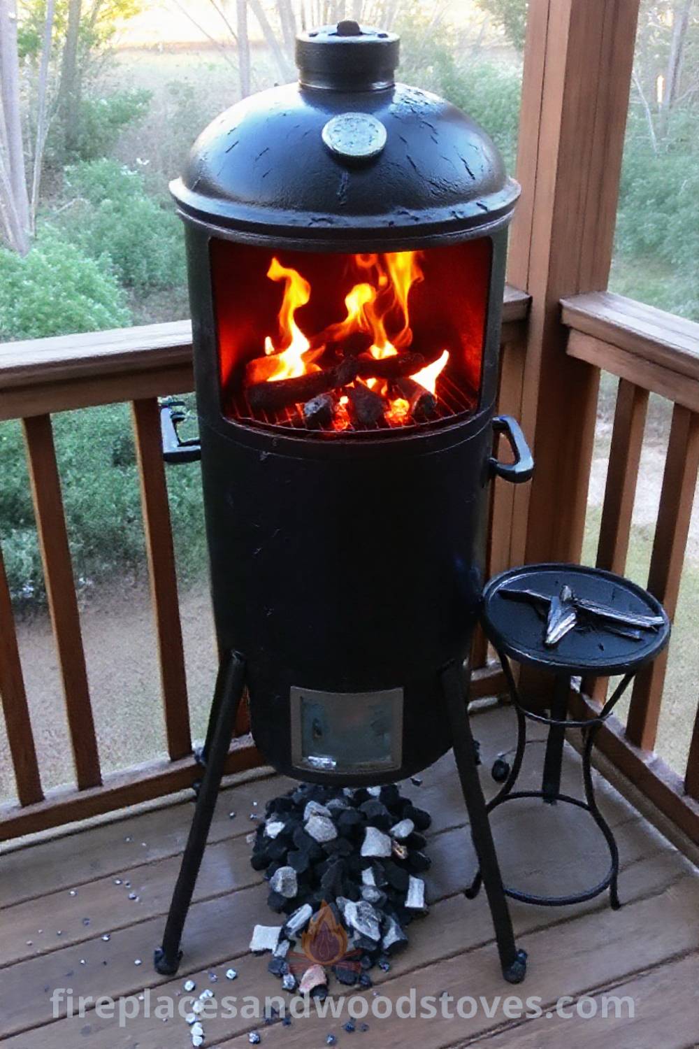 Vertical smoker barbecue on a wooden deck with flames flickering, surrounded by a few charcoal briquettes, a small table with spices and grilling tools, creating a cozy and inviting outdoor cooking space. Visit patioandhomefurniture.com for stylish ideas that will wow your guests.