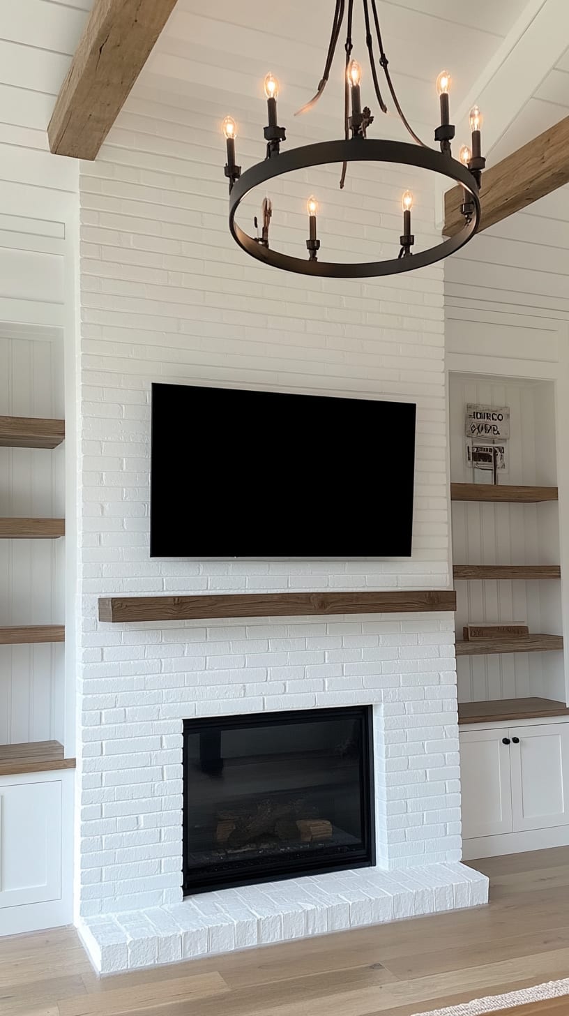 A cozy living room featuring a white brick fireplace with built-in shelves, a TV above, rustic wooden beams, and a large chandelier.