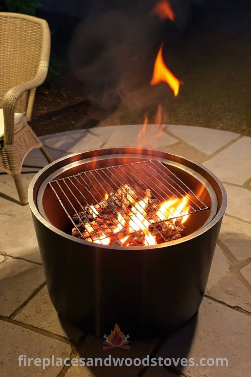 Sleek metal fire pit with a charcoal-burning grill grate on a stone patio, illuminating the area with flickering flames, creating a cozy atmosphere for outdoor cooking and gatherings. Visit patioandhomefurniture.com for incredible ideas that will wow your guests.