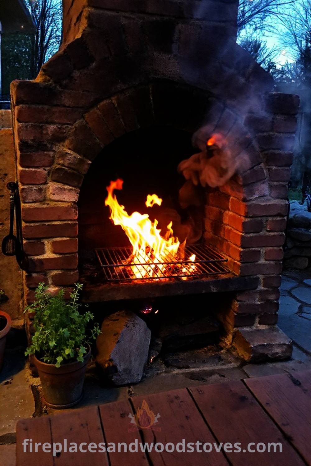 Rustic fireplace BBQ on a stone patio with weathered bricks and flickering flames, surrounded by potted herbs and a wooden table, creating a cozy and inviting outdoor atmosphere perfect for gatherings. Visit patioandhomefurniture.com for stylish designs transforming your backyard.