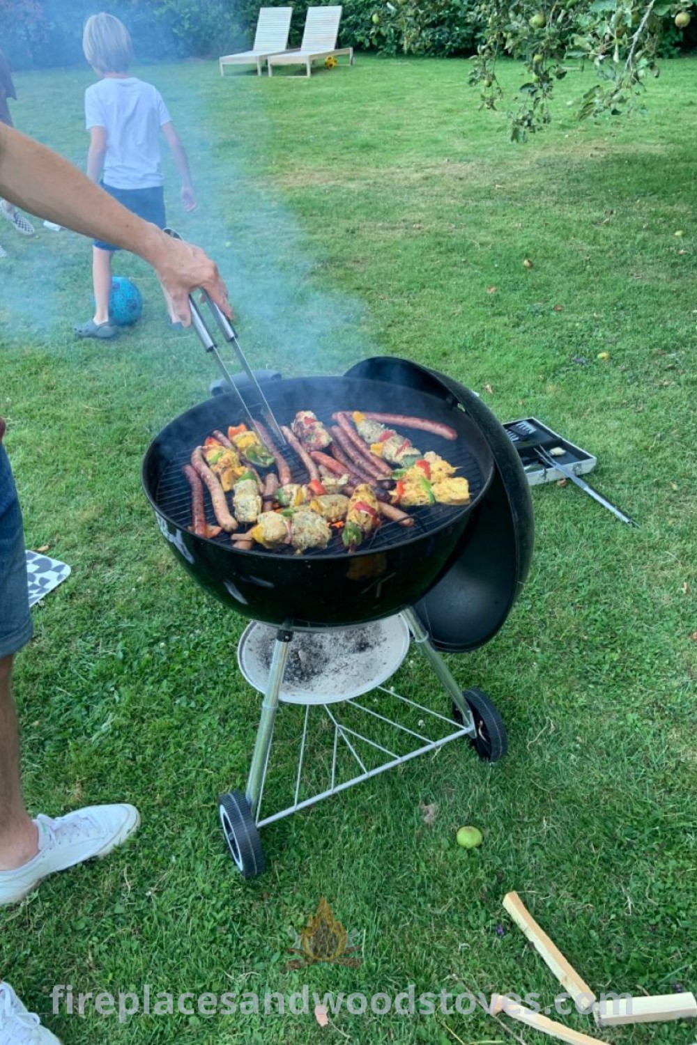 A man grilling food at a BBQ in the grass surrounded by people, showcasing summer vibes and stylish outdoor gathering ideas. Perfect for a 20th birthday or Fourth of July celebration. Discover more inspiration for your backyard at patioandhomefurniture.com.