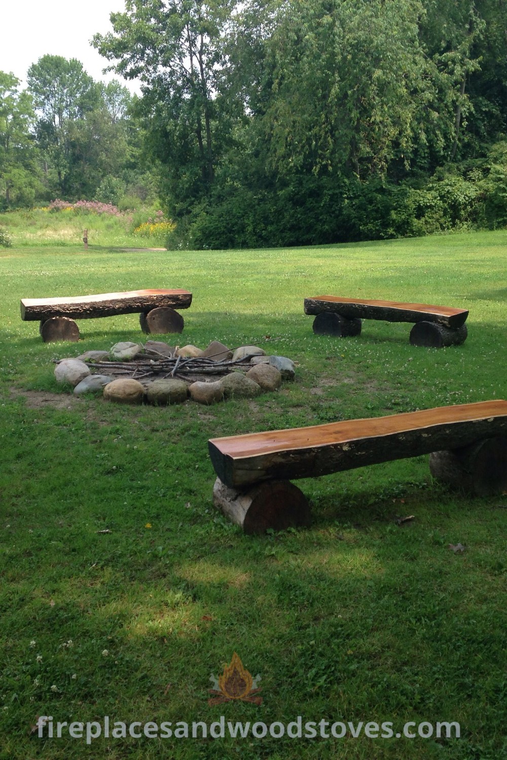 A fire pit surrounded by benches in a grassy area with trees, showcasing a cozy outdoor setup perfect for gatherings. Transform your backyard into a cottage homestead with stylish designs. Find DIY ideas and inspiration at patioandhomefurniture.com.