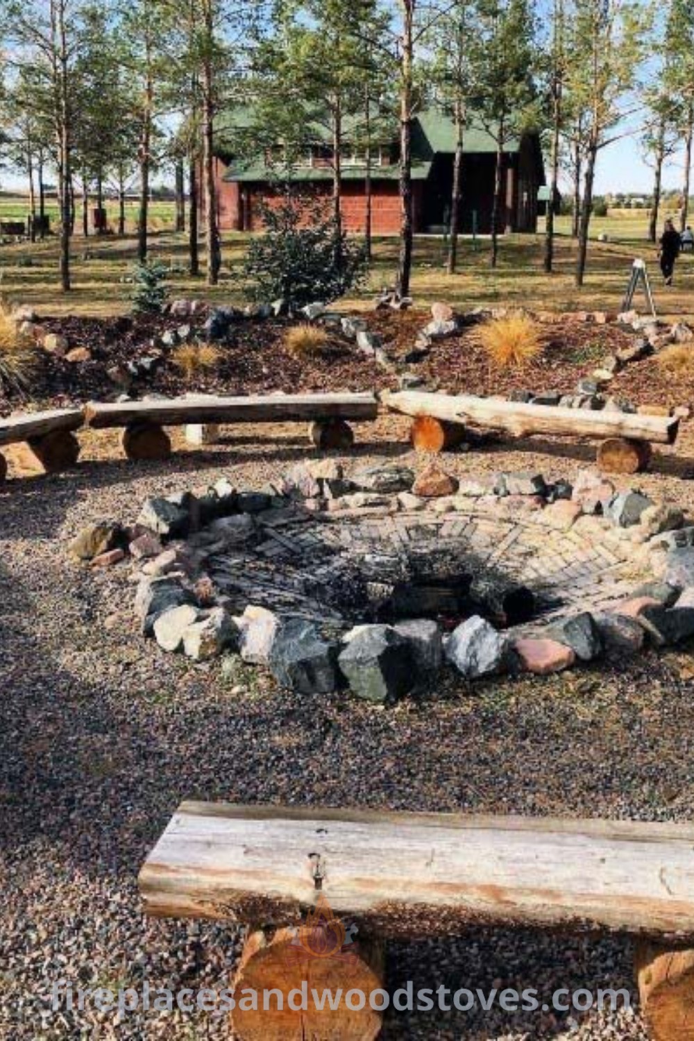 An outdoor fire pit surrounded by rustic benches and logs in a park area, showcasing stylish fire pit landscaping ideas and designs that enhance backyard gatherings. Find more inspiring outdoor ideas at patioandhomefurniture.com.