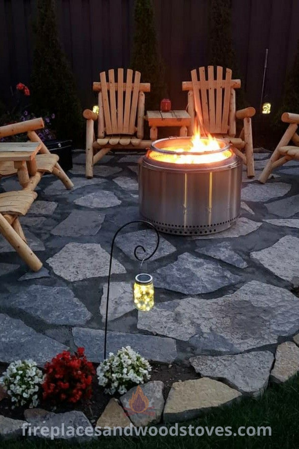 A cozy flagstone fire pit surrounded by lawn chairs and flowers, ideal for evening relaxation. This stylish setup offers ideas for enhancing your outdoor living space and gathering moments. Discover more at patioandhomefurniture.com.