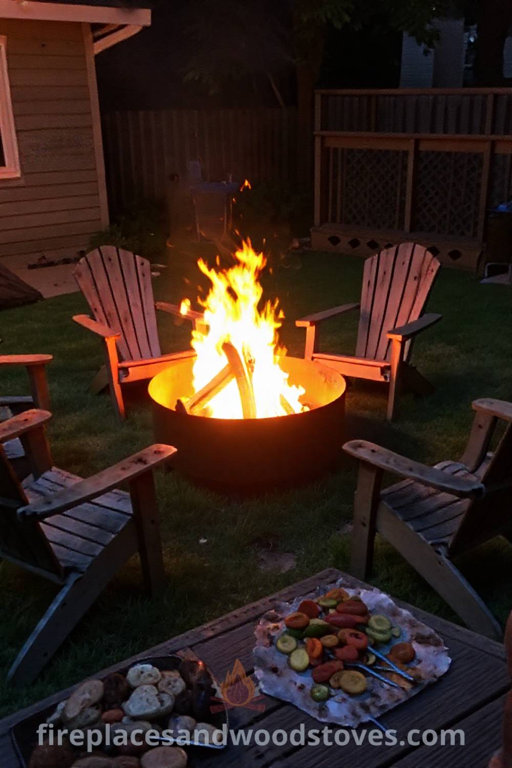 Sturdy metal wood-fired fire pit surrounded by worn wooden chairs in a cozy backyard, enhancing summer gatherings with grilled vegetables and warm glow. Visit patioandhomefurniture.com for stylish outdoor design ideas that will wow your guests.