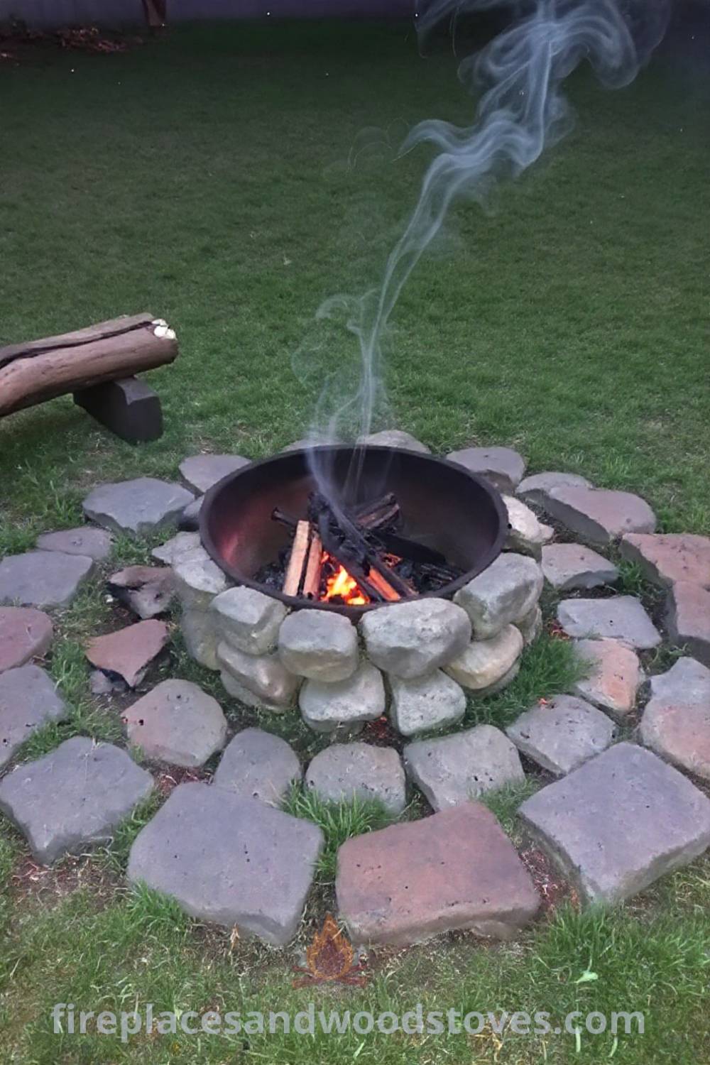 Rustic charcoal camping fire pit in a grassy backyard surrounded by stones and logs, creating a warm and inviting atmosphere for gatherings. Visit patioandhomefurniture.com for stylish outdoor ideas that will wow your guests.