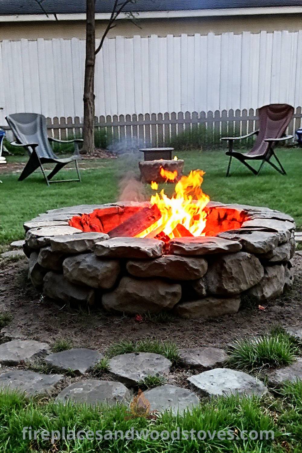 Cozy backyard camping setup featuring a stone fire pit with crackling flames, surrounded by worn camping chairs, and unevenly mowed grass, creating a warm and inviting outdoor space for gatherings. Visit patioandhomefurniture.com for incredible ideas transforming your backyard.