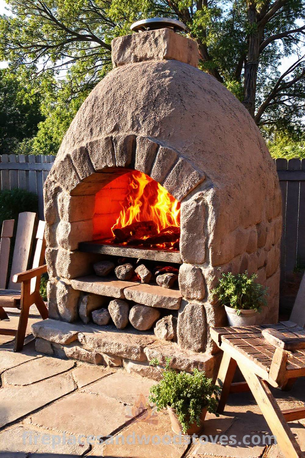 Sturdy stone BBQ oven on a sun-soaked patio, surrounded by potted herbs, rustic wooden chairs, and the warm glow of flames, creating a cozy atmosphere for outdoor gatherings. Visit patioandhomefurniture.com for incredible ideas to transform your backyard.