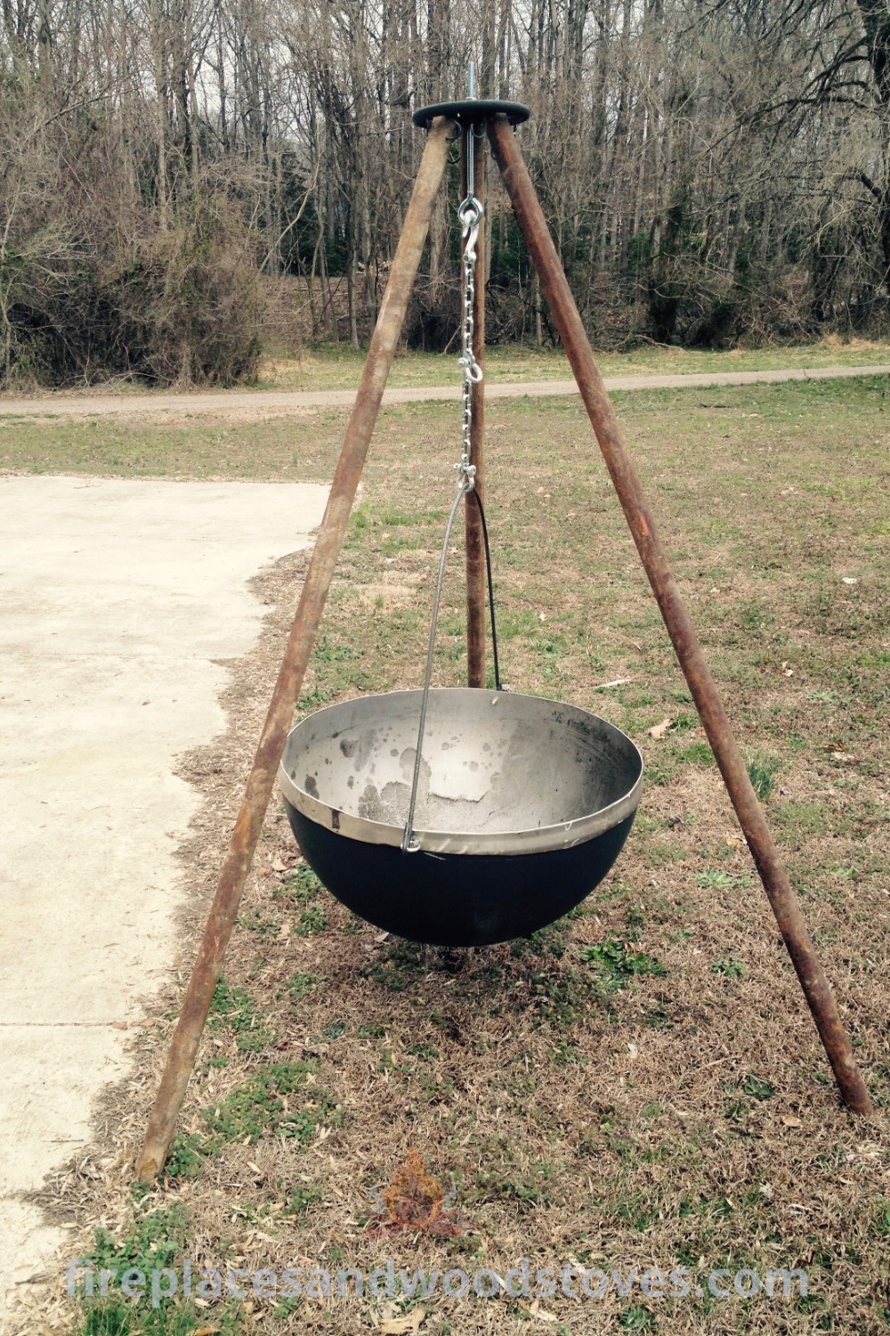An old metal bowl with wooden poles in the grass, ideal for creating a cozy bonfire pit or enhancing backyard decor. Perfect for stylish landscaping ideas and outdoor grill projects, discover more inspiration at patioandhomefurniture.com.