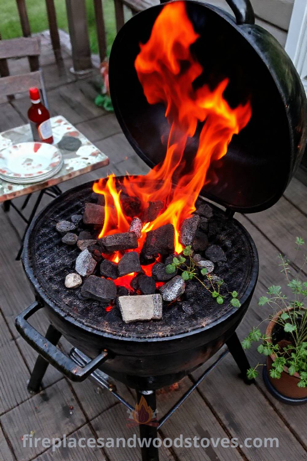 Classic charcoal grill on a weathered wooden deck with vibrant flames, casual table setting with mismatched plates, and potted herbs, creating a cozy outdoor barbecue scene. Visit patioandhomefurniture.com for stylish ideas that will wow your guests.