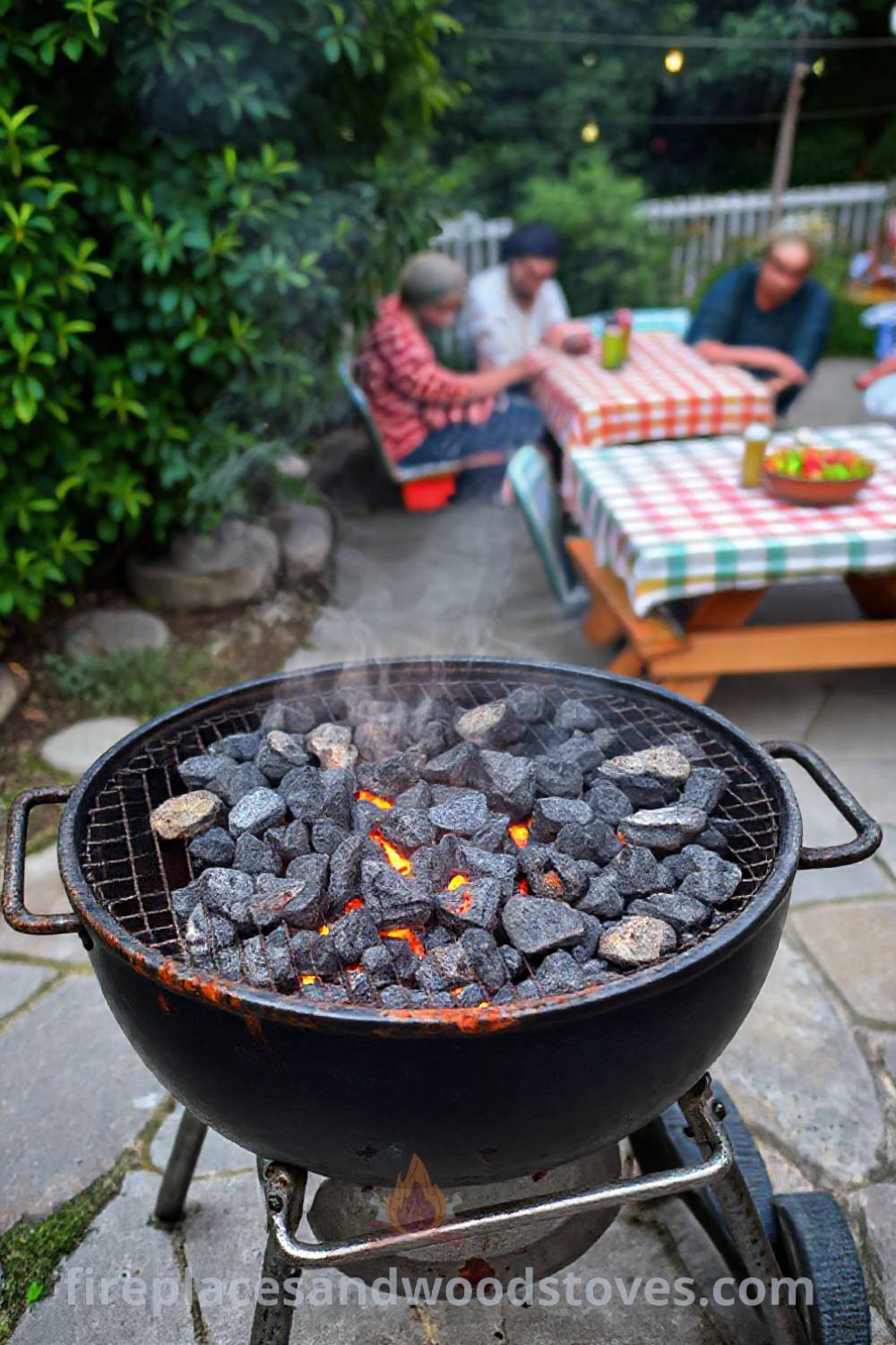Outdoor barbecue grill on a stone patio with glowing charcoal, colorful picnic tables with checkered cloths, and lush greenery, creating a cozy summer atmosphere for gatherings with friends. Visit patioandhomefurniture.com for stylish outdoor design ideas that will wow your guests.