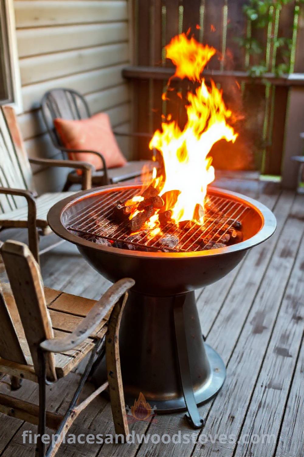 Metal charcoal-burning fire pit on a cozy patio with weathered wood deck and mismatched chairs, creating a warm gathering spot perfect for summer cookouts. Visit patioandhomefurniture.com for stylish outdoor design ideas.