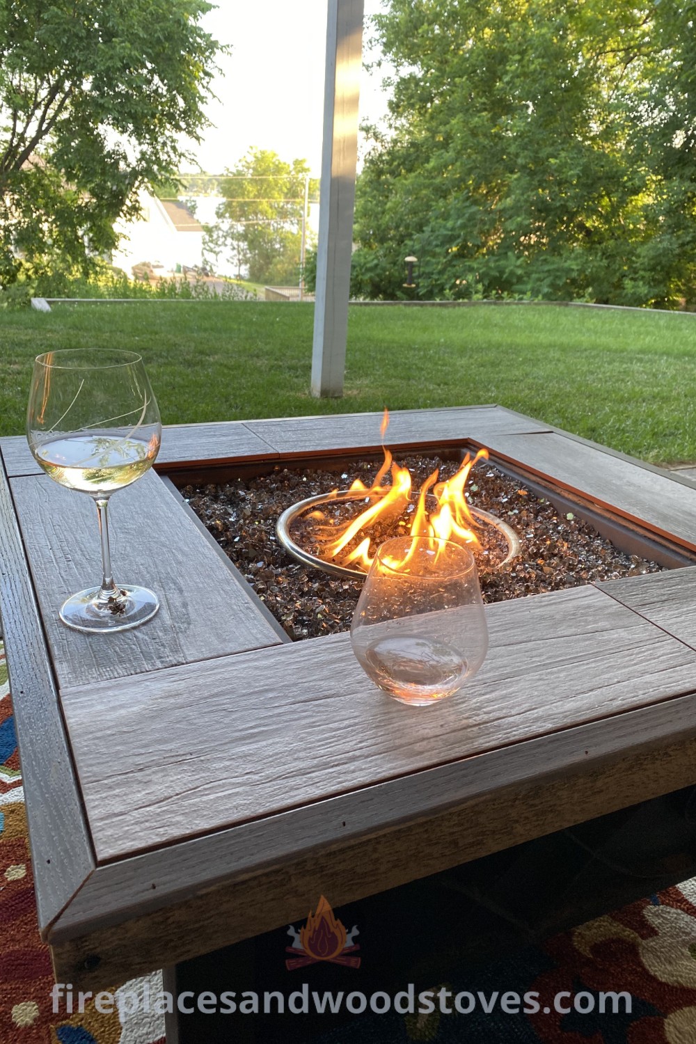 A fire pit table sitting on top of a wooden table next to a glass of wine, creating a cozy outdoor ambiance. Explore stylish outdoor fire pit ideas that will wow your guests at patioandhomefurniture.com.