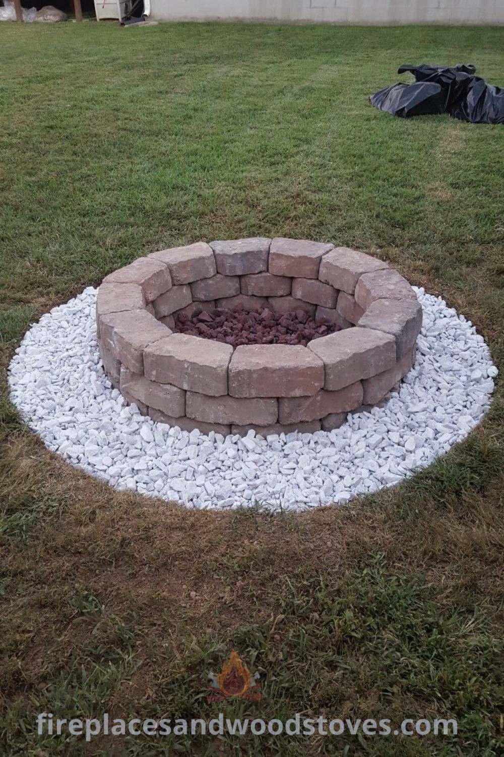 A fire pit in the center of a yard with gravel and grass, showcasing stylish design and incredible ideas for backyard fire pits on a budget. Discover more amazing outdoor ideas at patioandhomefurniture.com.
