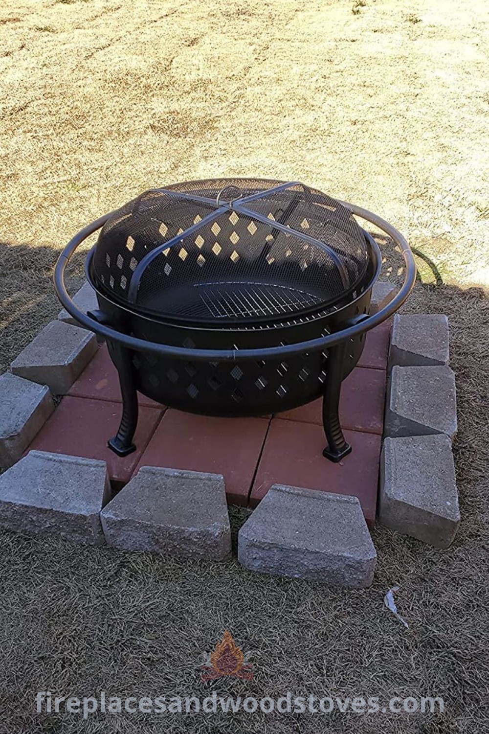 A black fire pit on a red brick patio beside a grass-covered field, showcasing stylish and cozy backyard fire pit ideas. Ideal for small spaces and rentals, perfect for evening gatherings. Discover more incredible outdoor ideas at patioandhomefurniture.com.