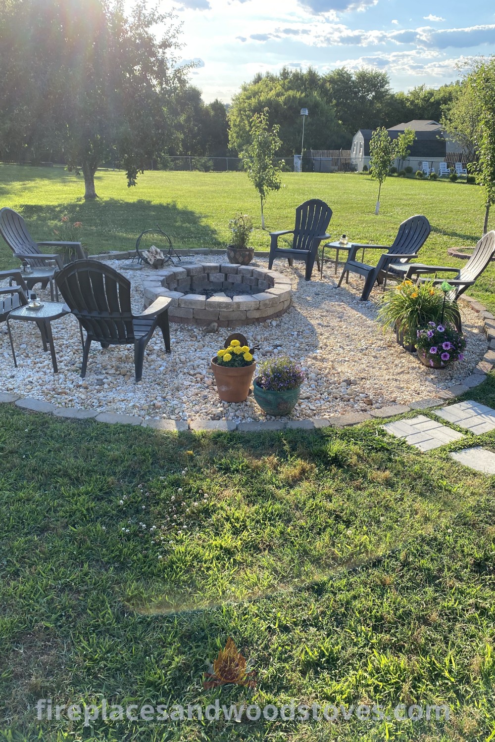 A cozy fire pit seating area surrounded by lawn chairs, flowers, and a flagstone pathway, creating a stylish and inviting outdoor space. Discover more incredible ideas for your backyard at patioandhomefurniture.com.