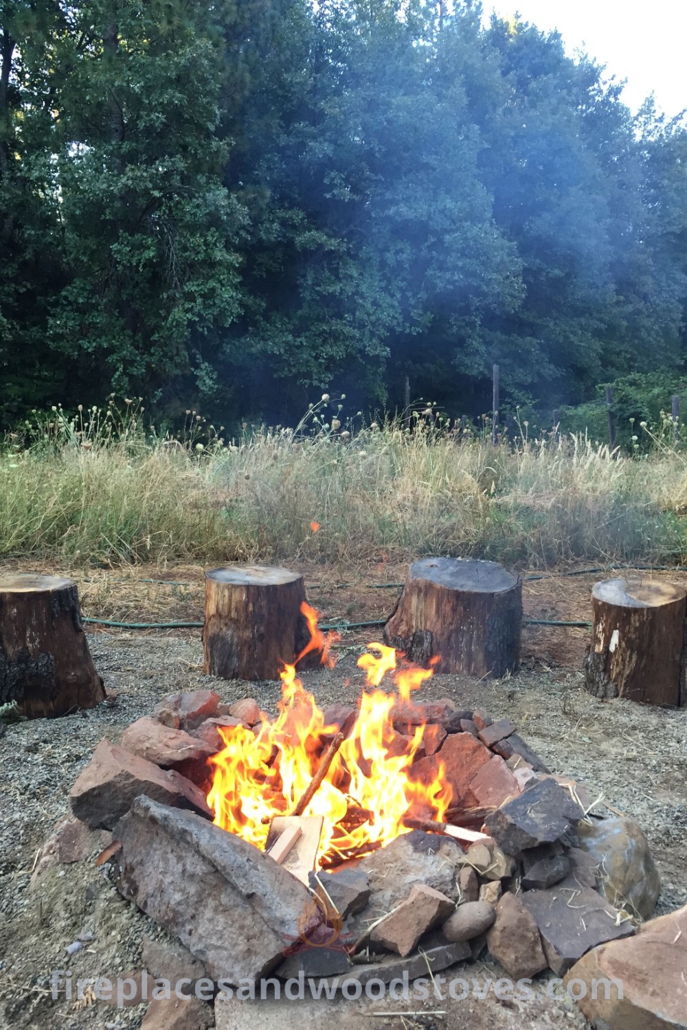 A cozy campfire in the middle of a field, surrounded by logs and firewood, demonstrating stylish outdoor fire pit designs ideal for backyard bonfires. Discover creative ideas for transforming your outdoor spaces at patioandhomefurniture.com.