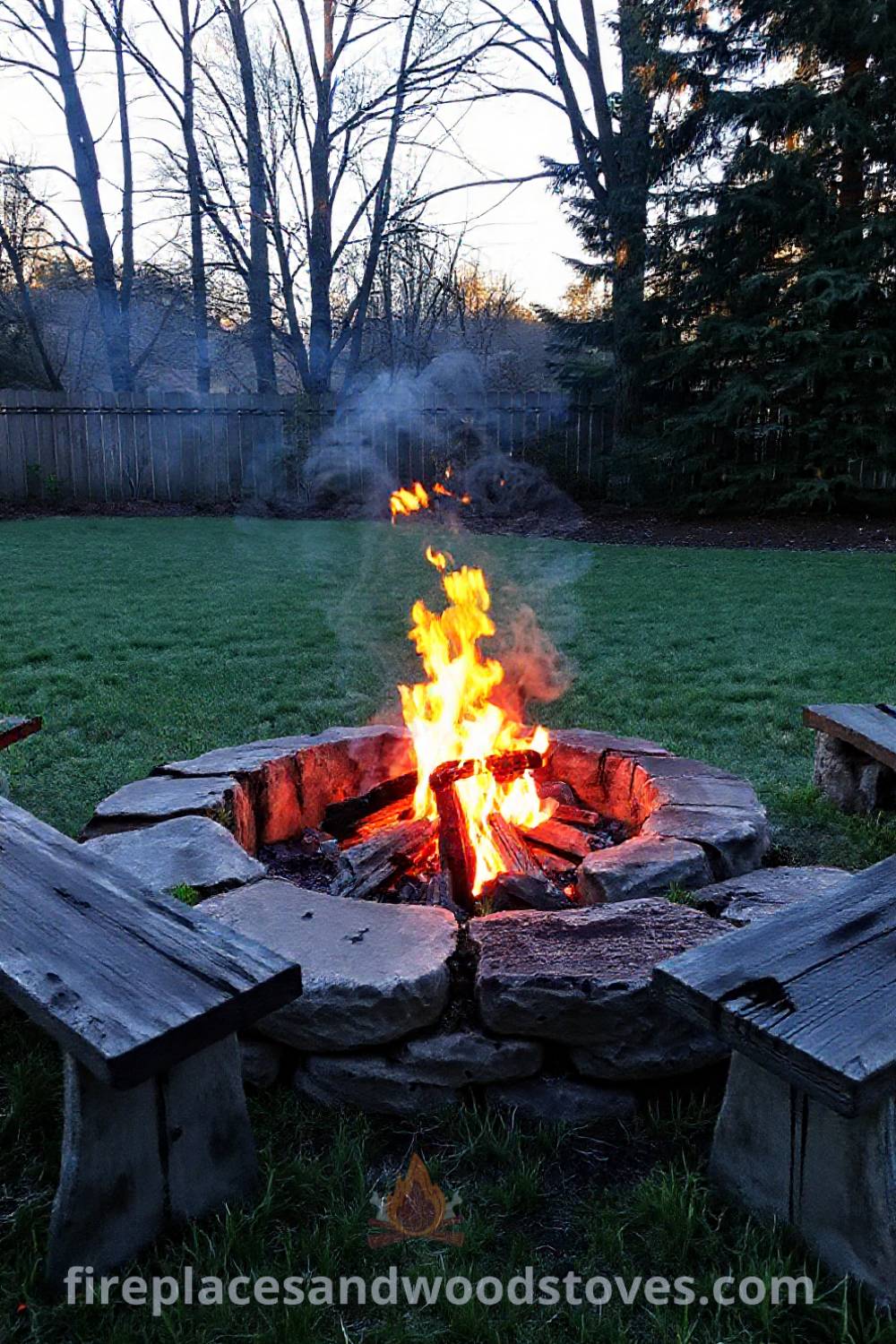 Outdoor cozy fire pit made of rough-hewn stone surrounded by aged wooden benches, flames illuminating nearby trees, creating a warm and inviting atmosphere for gatherings. Visit patioandhomefurniture.com for incredible ideas that will wow your guests.