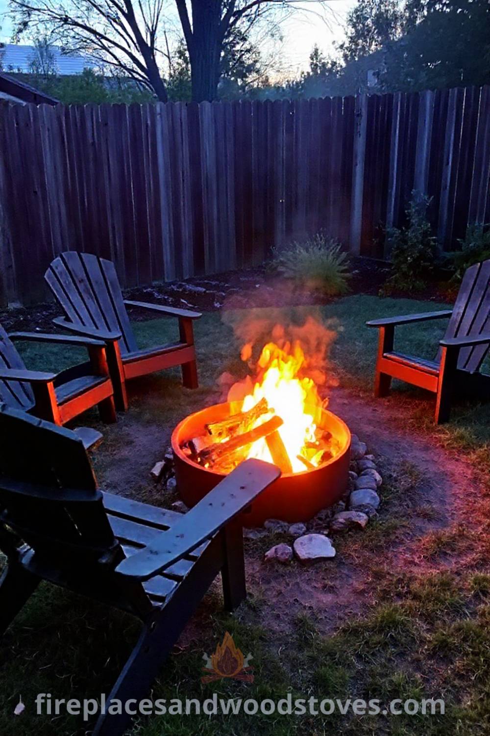 Cozy charcoal camping fire pit surrounded by adirondack chairs on uneven grass, glowing embers lighting the evening, perfect for outdoor gatherings. Visit patioandhomefurniture.com for stylish backyard design inspiration.